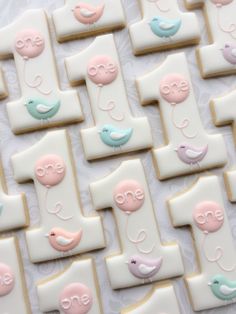 decorated cookies are arranged in rows on a white tablecloth with pink, blue and green decorations