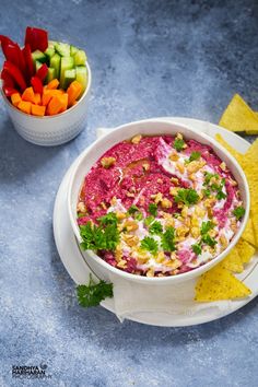 a white bowl filled with dip surrounded by chips and veggies