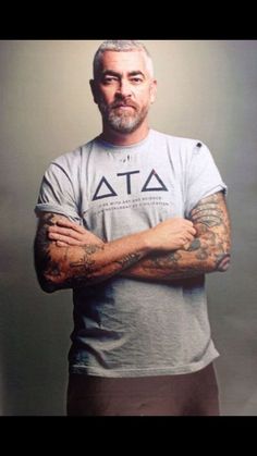 a man with tattoos standing in front of a gray background