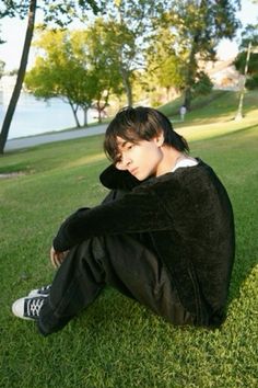 a young man sitting on the grass in front of trees