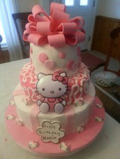 a three tiered cake with hello kitty on the top and pink bows around it