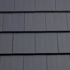 a clock on the side of a building with dark shingles and black roof tiles