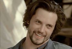 a close up of a person wearing a denim shirt and tie smiling at the camera