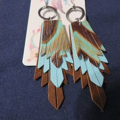 two pairs of brown and blue feather earrings on top of a white card with a tag