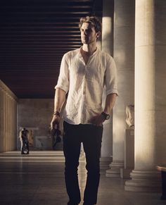 a man in white shirt and black pants standing next to columns