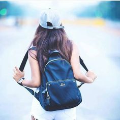 a woman with a back pack walking down the street holding her hand in her pocket