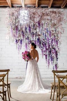 a woman in a wedding dress standing next to chairs with flowers hanging from the ceiling