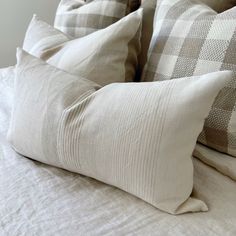 four pillows on top of a bed with white sheets and checkered pillowcases