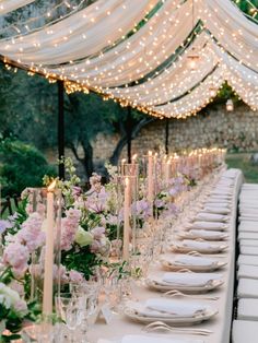 a long table is set with white and pink flowers, candles, and place settings