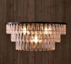 a chandelier hanging from a wooden wall with glass drops on the bottom and sides