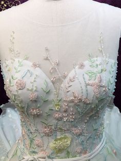 the back of a white dress with flowers on it and green trim around the bust