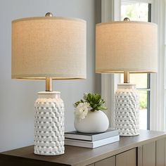 two white vases sitting on top of a table next to each other with lamps