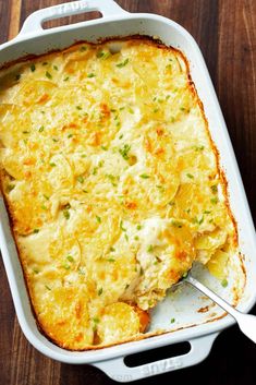 a casserole dish with chicken and cheese in it on a wooden table next to a fork