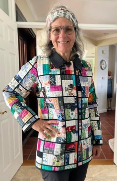 an older woman standing in front of a door wearing glasses and a colorful jacket with patches on it