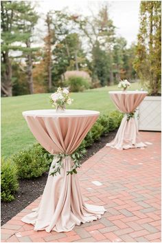 two tables covered in pink cloths with flowers on each table and greenery at the top