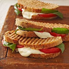 two grilled sandwiches with tomatoes, mozzarella and basil on a wooden cutting board