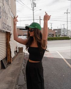 Beautiful hot stylish skinny girl with dark chocolate brown hair wearing a black spaghetti strap tank top, black trousers and an emerald green New York NYC Yankees baseball hate giving the camera the finger with both hands. She is wearing street wear street style Outfits With Green Hats For Women, Dark Green Hat Outfit, Green Baseball Hat Outfit, Green Cap Outfit, Green Hat Outfit, Green Trousers Outfit, Black Street Style, Trouser Fashion, Baseball Hat Outfit