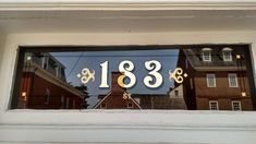 the reflection of two buildings in a window with gold numbers on it's side