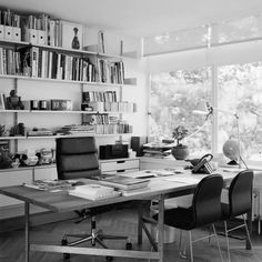 a desk with two chairs and bookshelves in front of a window