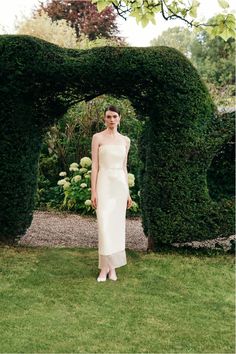 a woman standing in front of a hedge archway