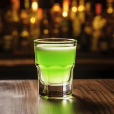 a green drink sitting on top of a wooden table in front of a blurry bar