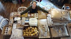 a woman sitting at a table surrounded by boxes and bags filled with potatoes on it