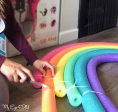 a woman sitting on the floor with some scissors in her hand and rainbow colored tube next to it