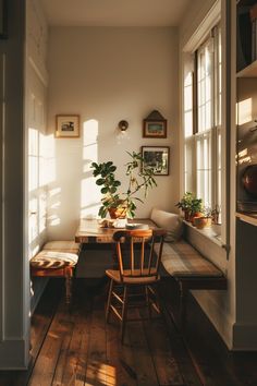 a dining room table with two chairs and a bench in front of the window, next to a potted plant