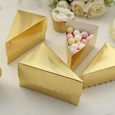 gold boxes with candy in them sitting on a table next to flowers and cupcakes