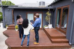 three people standing on steps in front of a house looking up at the roof and door