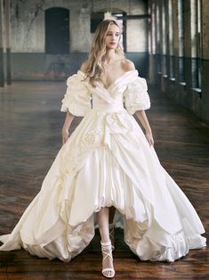 a woman in a white wedding dress standing on a wooden floor with her arms behind her back