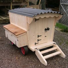 a small wooden cart with a metal roof and red wheels on gravel area next to building