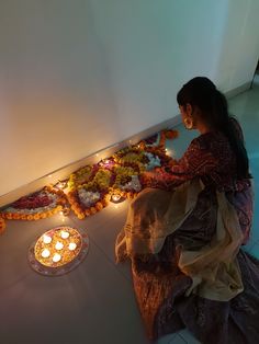 a woman sitting on the floor in front of flowers and candles with lights around her