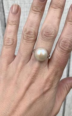 This elegant and stately pearl ring is made from a beautiful and unique white cream 14mm Mabe South Sea AAA Pearl that has many hues including pink. The pearl has been set in sterling silver with a sterling silver ring band handmade from half dome wire. This ring has some height, the setting is almost 1/2 inch high. The white cream pearl is more matte than the other mabe pearls listed, but still has a luminescent quality that makes it captivating!Made to order! Choose your size and your color pe White Mother Of Pearl Wedding Ring, Elegant Round Mother Of Pearl Ring, Classic Mother Of Pearl Ring As Gift, Classic Mother Of Pearl Ring As A Gift, Wedding Pearl Ring In Mother Of Pearl, Classic Mother Of Pearl Ring For Gift, Elegant White Mother Of Pearl Ring, Elegant Mother Of Pearl Ring As Gift, Wedding Pearl Ring With Mother Of Pearl