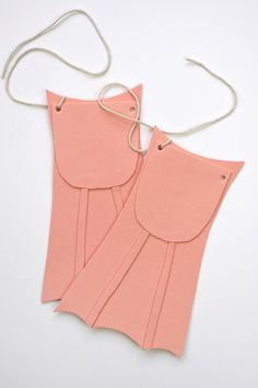 two pieces of pink paper with tags attached to them on a white surface, one piece is cut out and the other part has been folded