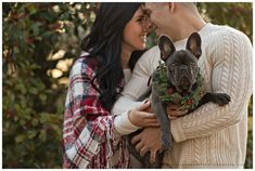 a man and woman holding a dog wearing a wreath on it's head while standing next to each other