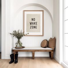 a wooden bench sitting in front of a white wall with a framed poster above it