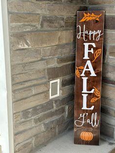 a wooden sign that says happy fall and is next to a brick wall with pumpkins on it