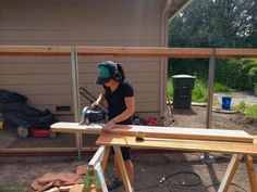 a woman is using a circular saw to cut planks on a wooden table outside