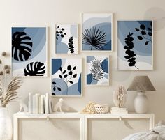 a white table topped with vases filled with flowers and plants next to pictures on the wall