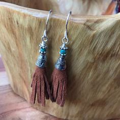 a pair of earrings with tassels on top of a wooden table next to a plant