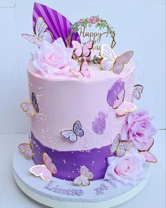 a pink and purple birthday cake with butterflies on the top is decorated with flowers, roses, and a happy birthday sign