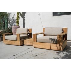 two wooden chairs sitting next to each other on a cement floor near a building with cactus in the background