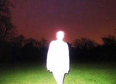 a man standing in the middle of a field at night with his back turned to the camera