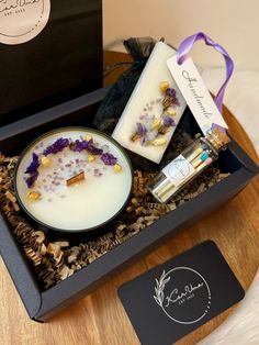 a candle and some flowers in a black box on a table with a purple ribbon