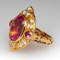 This designer Paula Crevoshay ring is centered with one (1), bezel set, oval mixed cut natural pink tourmaline and is bordered with two (2), bezel set, round mixed cut natural pink tourmalines and fourteen (14), bezel/ bead set, round brilliant cut diamonds. The top half of the tapered shank features a pierced design. The ring measures 28.9mm at the top, rises 8.9mm above the finger, tapering to 4.0mm wide and 1.2mm thick at the base of the shank. It is currently a size 6.75. Luxury Tourmaline Rings With Rose Cut Diamonds, Pink Oval Multi-stone Ruby Ring, Oval Tourmaline Ruby Ring For Formal Occasions, Formal Oval Tourmaline Ruby Ring, Formal Oval Ruby Ring With Tourmaline, Luxury Oval Tourmaline Ring, Formal Multi-stone Ruby Ring With Tourmaline, Pink Oval Ruby Ring With Gemstone Accents, Luxury Oval Sapphire Ring With Bezel Setting