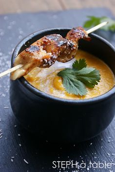 a black bowl filled with soup and meat skewers