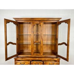 an old fashioned wooden china cabinet with glass doors and drawers on the bottom, in front of a white brick wall