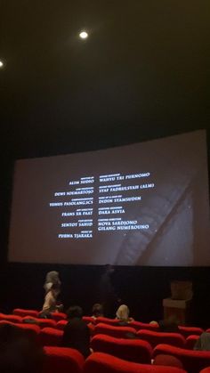 people are sitting in red chairs and watching a presentation on the screen at an auditorium