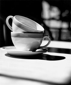 black and white photograph of two cups on a table with the reflection of another cup